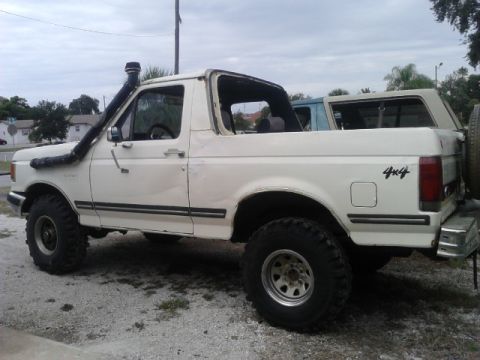 1988 Ford Bronco - A white Ford Bronco with a snorkel and off-road tires is parked on a gravel lot.