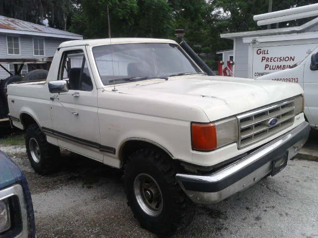 White Ford Bronco with off-road tires parked outdoors. The grille and headlights suggest an early 1990s model