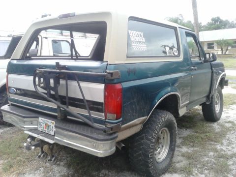 1996 Ford Bronco - Rear view of a 1996 Ford Bronco with a spare tire carrier and a partial view of another vehicle.