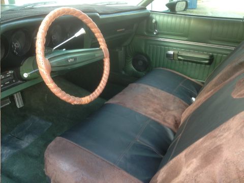 1973 Ford Ranchero - The interior of a car features green upholstery, a unique steering wheel cover, and dark and brown seat covers.