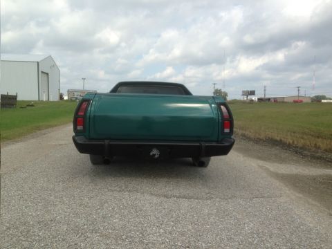 1973 Ford Ranchero - Rear view of a green pickup truck with a black bumper and dual exhaust pipes on a gravel road.