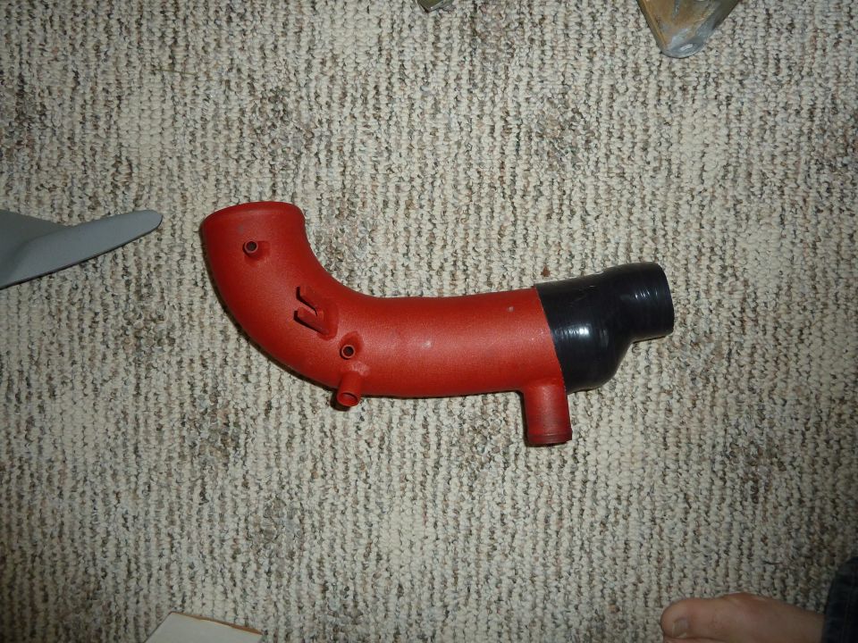 Red and black intake hose with two small nipples and a flange, lying on carpet