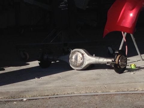 1964 Ford Fairlane - A rear axle assembly is shown on a concrete surface with a red car fender in the background.